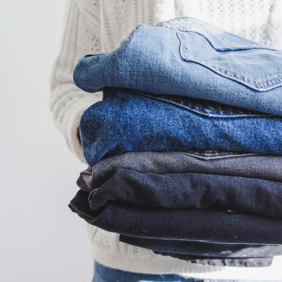 Ein Stapel gefalteter Altkleider, hauptsächlich Jeans in verschiedenen Blautönen von hell bis dunkel, aufgetürmt auf einem hellen Untergrund.